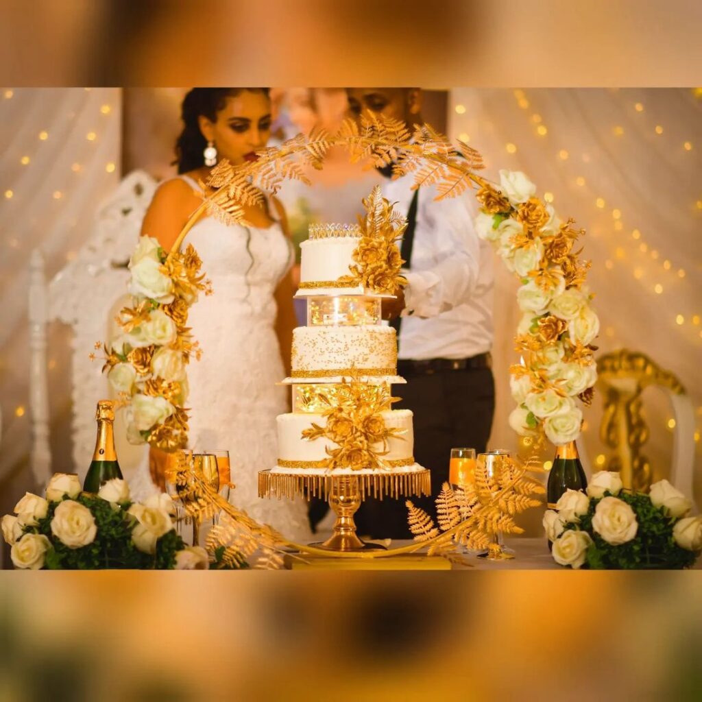Tiered white wedding cake at a wedding reception, framed by a floral arch